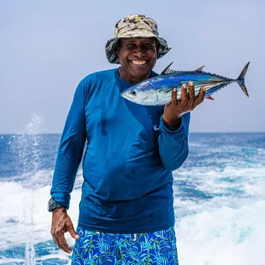 Smiling fisherman holding freshly caught tuna in open sea